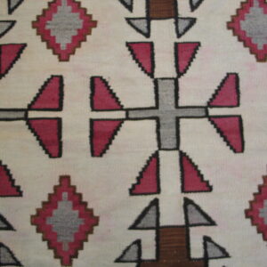 Flatweave rug with geometric pink, grey, and brown cross and diamond motifs on a cream background.