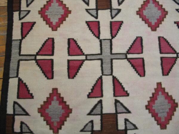Flatweave rug with geometric pink, grey, and brown cross and diamond motifs on a cream background.