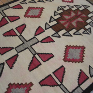 Geometric flatweave rug in cream, red, brown, and gray on distressed wooden plank flooring.