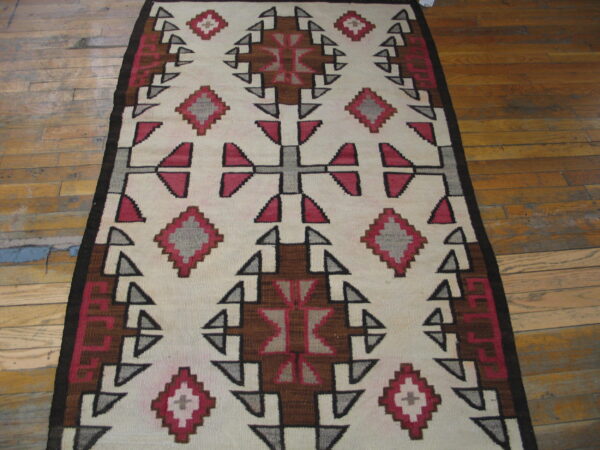 Geometric flatweave rug in cream, red, brown, and gray on light brown distressed wood flooring.