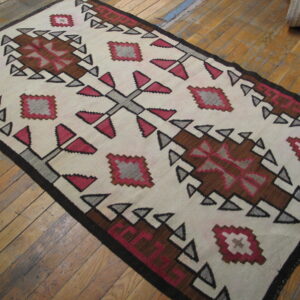 Cream flatweave rug with dark brown and pink geometric medallions lies on light wood flooring.
