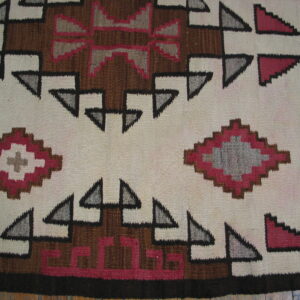Geometric flatweave rug featuring stepped patterns in cream, brown, gray, and magenta, resting on wood planks.