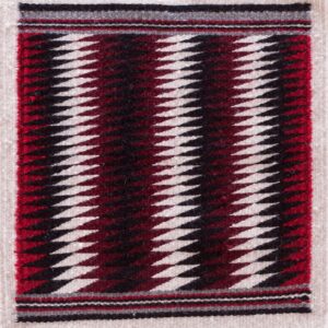 Small flat-weave rug featuring cream, black, red, and maroon serrated diamond stripes on wood floor.
