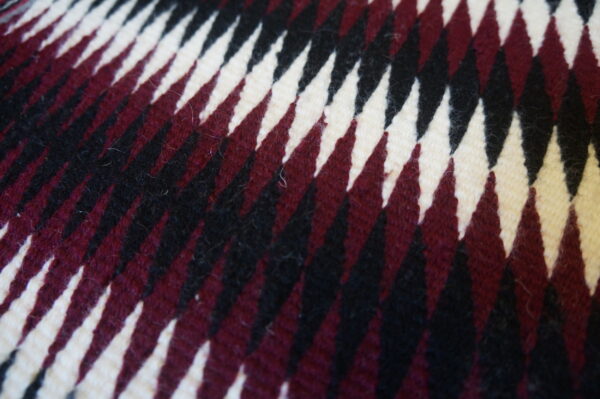 Antique allover geometric wool flat weave multicolor jewel tones 1930s square rug 2 Close-up of a square rug with sharp, diagonal zigzags in cream, burgundy, and black fibers.