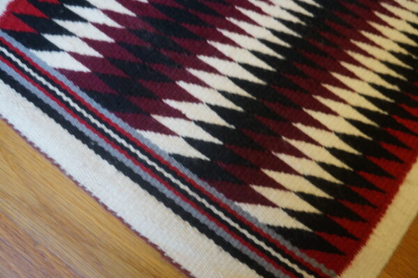 Antique allover geometric wool flat weave multicolor jewel tones 1930s square rug 3 Square flatwoven rug featuring a burgundy, black, and cream serrated diamond pattern on hardwood flooring.