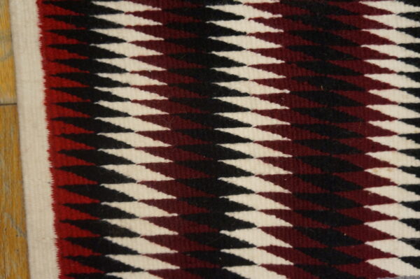 Antique allover geometric wool flat weave multicolor jewel tones 1930s square rug 5 Low-pile square rug featuring interlocking geometric diamonds in cream, black, and deep maroon on wood flooring.