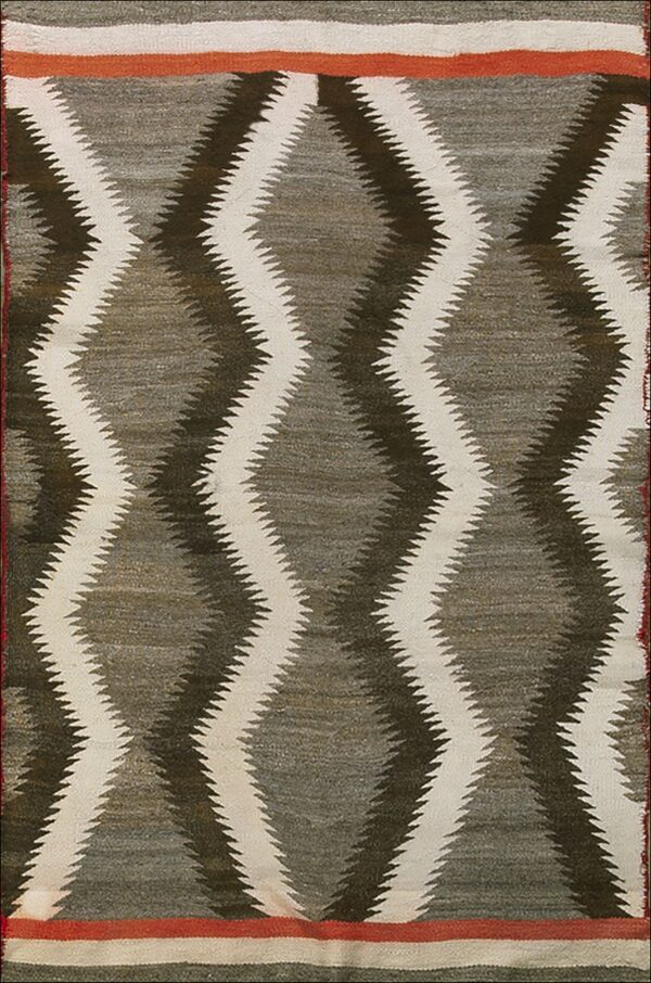 Flatweave textile with cream and dark serrated diamond motifs on a taupe background, framed by rust and white stripes.