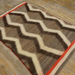 Brown and cream zig-zag rug with an orange border strip rests on aged hardwood plank flooring.