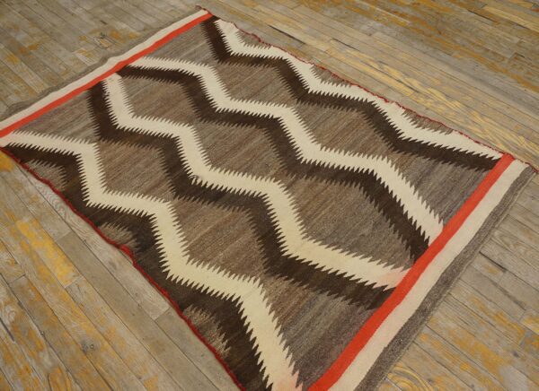 Brown and cream zig-zag rug with an orange border strip rests on aged hardwood plank flooring.
