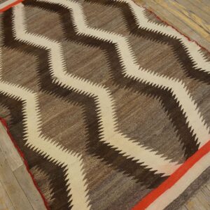 Brown and cream zigzag rug with orange stripe borders rests on faded wooden plank flooring.