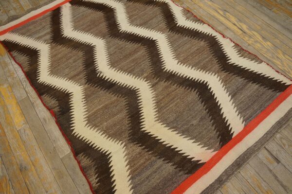 Brown and cream zigzag rug with orange stripe borders rests on faded wooden plank flooring.