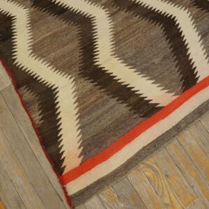 A flatweave rug featuring brown, grey, and cream zigzags and an orange stripe rests on distressed wood planks.