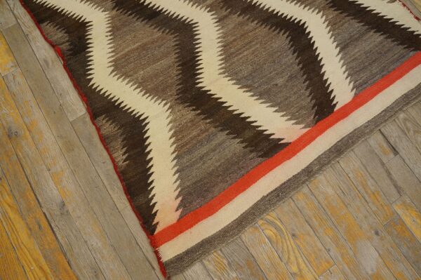 A flatweave rug featuring brown, grey, and cream zigzags and an orange stripe rests on distressed wood planks.