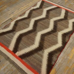 A flatweave rug with dark brown, tan, and cream serrated zigzags is laid on worn wood flooring.