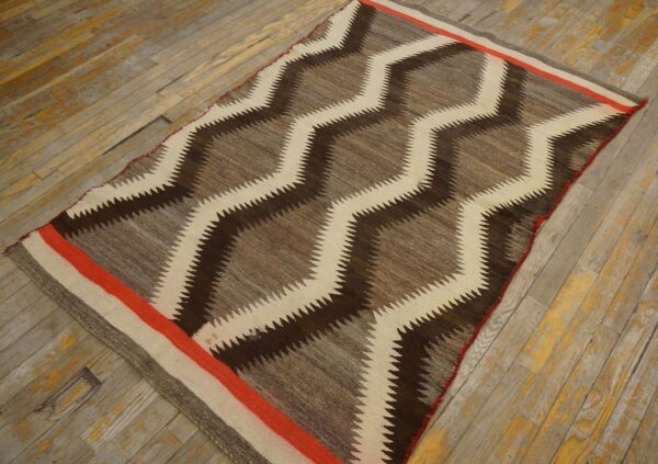 A flatweave rug with dark brown, tan, and cream serrated zigzags is laid on worn wood flooring.