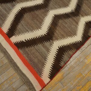 A brown, gray, and cream serrated diamond rug with an orange striped border on distressed wood.