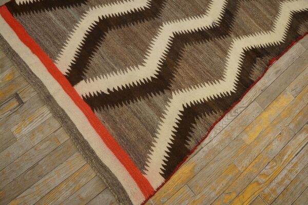 A brown, gray, and cream serrated diamond rug with an orange striped border on distressed wood.