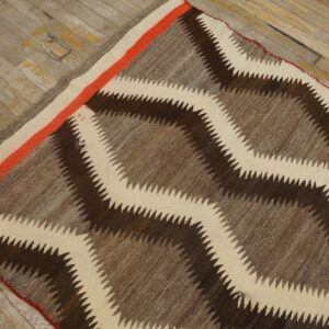 Serrated zigzag rug in brown and cream, featuring an orange accent stripe, resting on weathered wood.
