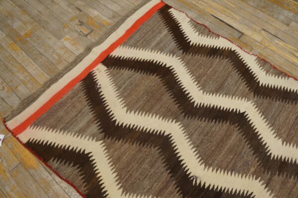 Serrated zigzag rug in brown and cream, featuring an orange accent stripe, resting on weathered wood.