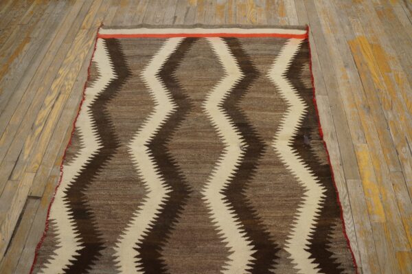 Brown and cream zigzag patterned flatweave rug accented with red, placed on yellowed wood floor.