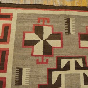 Geometric flat-weave rug in brown, cream, gray, and red resting on wide plank wood floors.