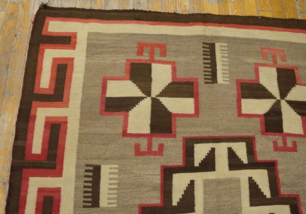 Geometric flat-weave rug in brown, cream, gray, and red resting on wide plank wood floors.
