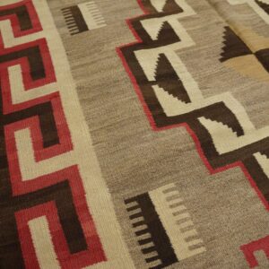 Geometric flat-weave rug in browns, cream, and red featuring stepped patterns on distressed wood flooring.