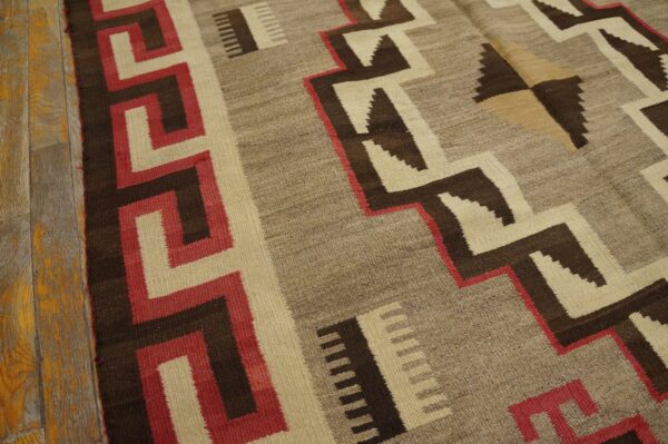 Geometric flat-weave rug in browns, cream, and red featuring stepped patterns on distressed wood flooring.