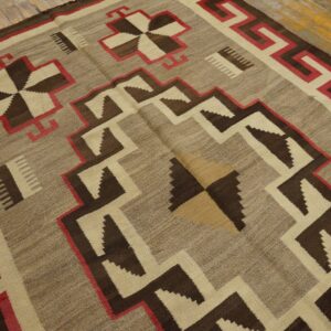 Flatweave rug with dark brown, taupe, cream, and red geometric patterns rests on wood flooring.