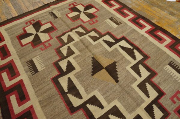 Flatweave rug with dark brown, taupe, cream, and red geometric patterns rests on wood flooring.