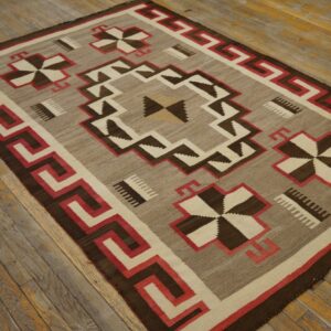 Tan, dark brown, red, and cream flat-weave rug with a geometric border rests on distressed wood flooring.