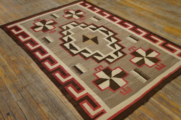 Tan, dark brown, red, and cream flat-weave rug with a geometric border rests on distressed wood flooring.