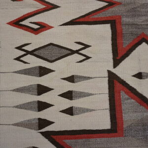Cream and gray flatweave rug with geometric red and brown patterns next to worn wood.
