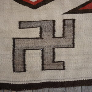 Geometric flatweave rug featuring cream, grayish-brown, and dark red patterns on a distressed wooden floor.