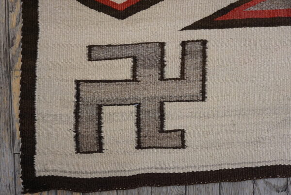 Geometric flatweave rug featuring cream, grayish-brown, and dark red patterns on a distressed wooden floor.