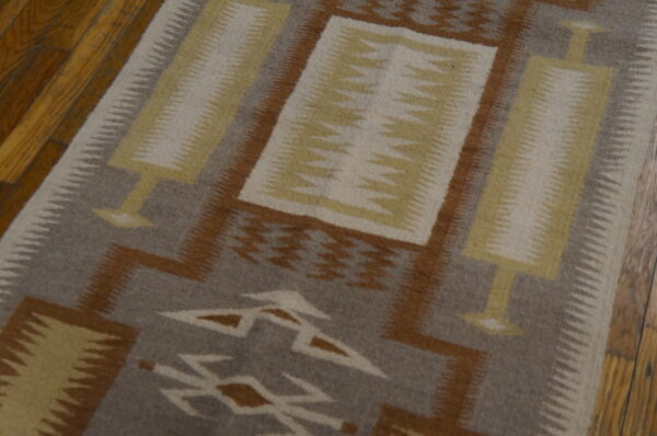 Geometric runner rug with gray, brown, yellow, and cream patterns on wooden floorboards.