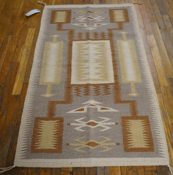 Geometric flatweave rug in gray, brown, and cream with serrated edges lying on dark hardwood flooring.