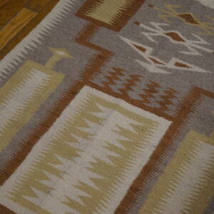 Flat woven rug with grey, brown, cream, and yellow geometric patterns on wooden floorboards.