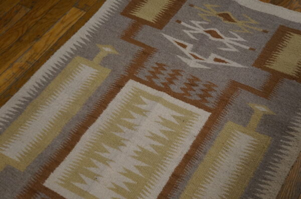 Flat woven rug with grey, brown, cream, and yellow geometric patterns on wooden floorboards.