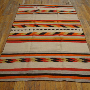 Low-profile rug featuring cream, orange, red, and black stripes with geometric patterns displayed on wood flooring.