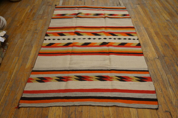 Low-profile rug featuring cream, orange, red, and black stripes with geometric patterns displayed on wood flooring.