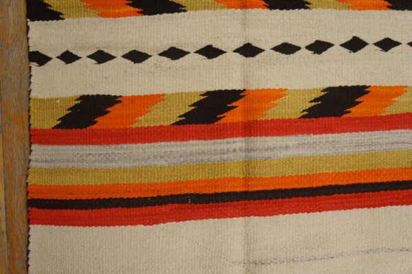 Striped flatweave rug displaying black diamonds, zigzags, and bands of red, orange, gold, and cream on wood.