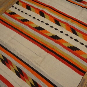 Flat-weave rug featuring cream, red, orange, black, and gold diagonal stripes on distressed wood flooring.