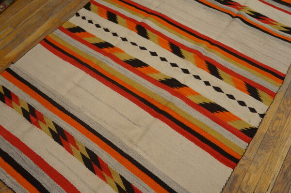 Flat-weave rug featuring cream, red, orange, black, and gold diagonal stripes on distressed wood flooring.