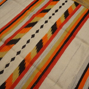 Flatweave rug with bright zigzag and diamond stripes in orange, red, black, and cream over wood floor.