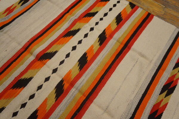 Flatweave rug with bright zigzag and diamond stripes in orange, red, black, and cream over wood floor.