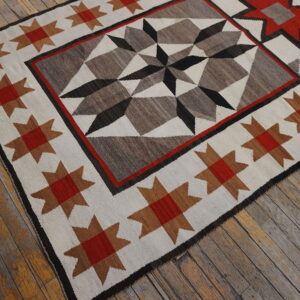 Flatweave rug with a tribal star motif in red, brown, gray, and black on worn wood floor.