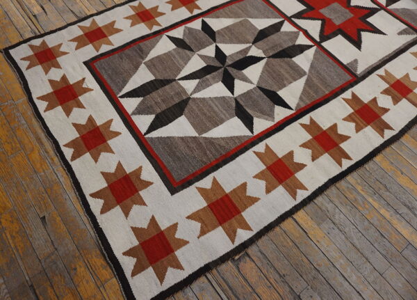 Flatweave rug with a tribal star motif in red, brown, gray, and black on worn wood floor.