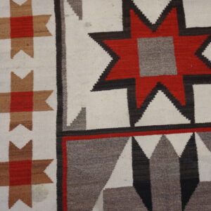 Geometric flatweave rug in white, red, tan, and gray featuring stars, displayed on distressed wood flooring.