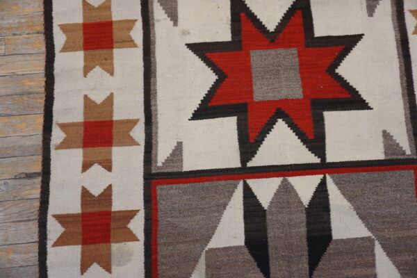 Geometric flatweave rug in white, red, tan, and gray featuring stars, displayed on distressed wood flooring.